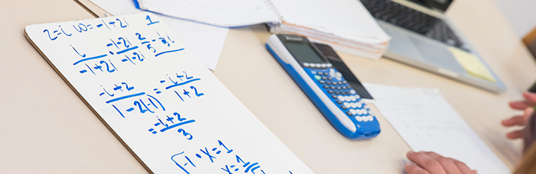 a table with paper, math equations, calculator, and a person's hands